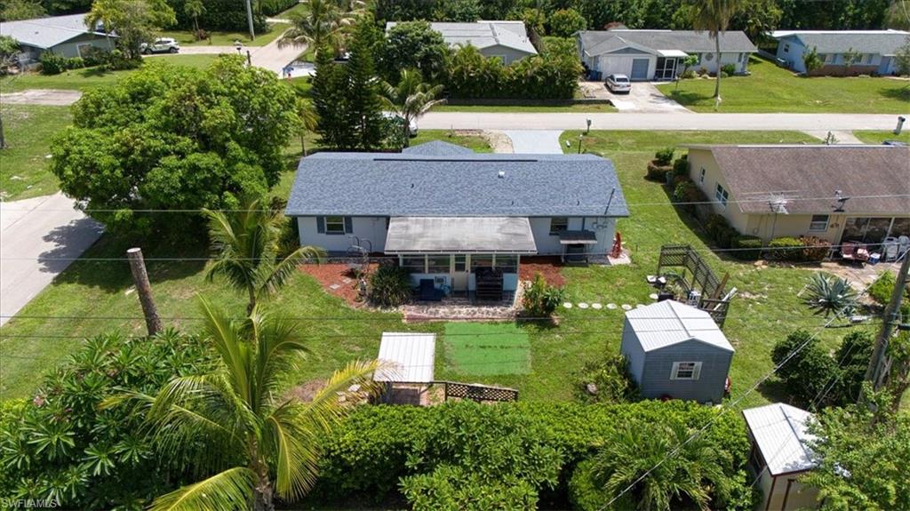 Single-story residence with a gray shingle roof, light-colored exterior, covered front porch, and a detached storage shed