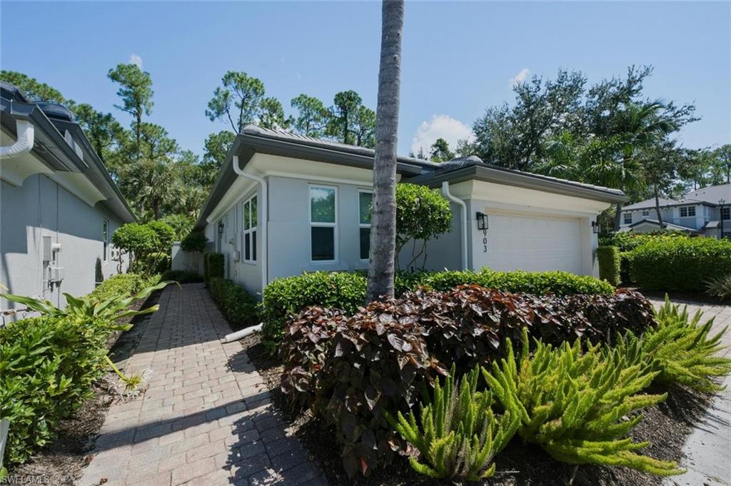 Contemporary exterior with an attached garage, paver walkway, lush landscaping, and a tile roof