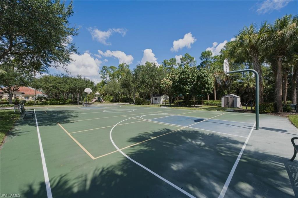 Multipurpose court with painted lines, two basketball hoops, surrounding trees, paved pathway, and benches