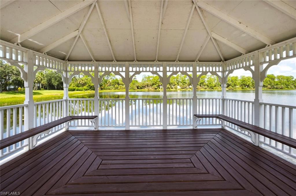 White gazebo with a dark wood-finish floor and integrated seating, featuring a gabled roof and decorative balusters