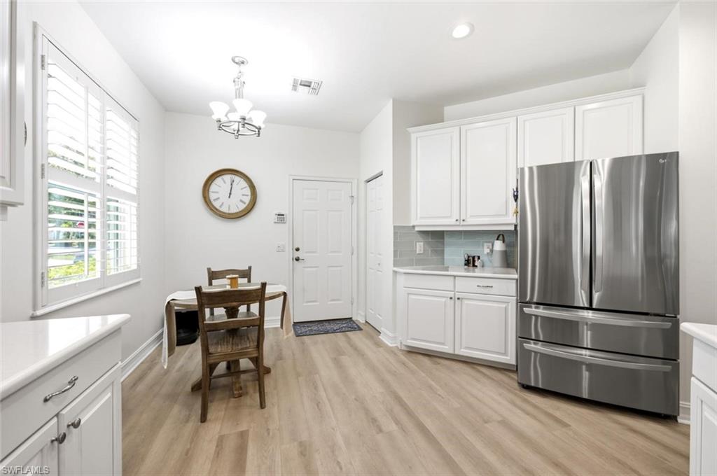White cabinetry with brushed nickel hardware, stainless steel refrigerator, light-toned wood-finish flooring, white plantation shutters, and a recessed ceiling light