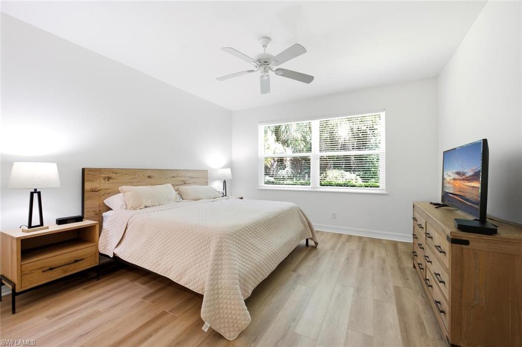 Wood-finish flooring, natural wood headboard, ceiling fan, wide impact window with blinds