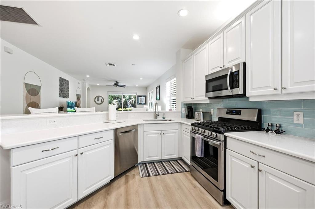 White shaker-style cabinetry with stainless steel hardware, light-toned wood-finish flooring, light-colored countertops, and a blue subway tile backsplash