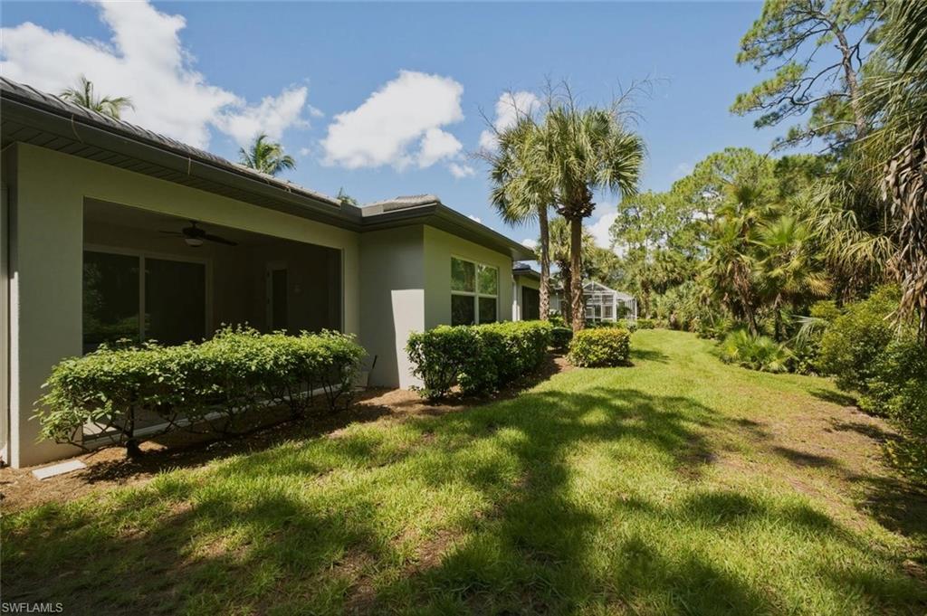 Covered patio with a ceiling fan and sliding glass doors, surrounded by lush landscaping and mature trees