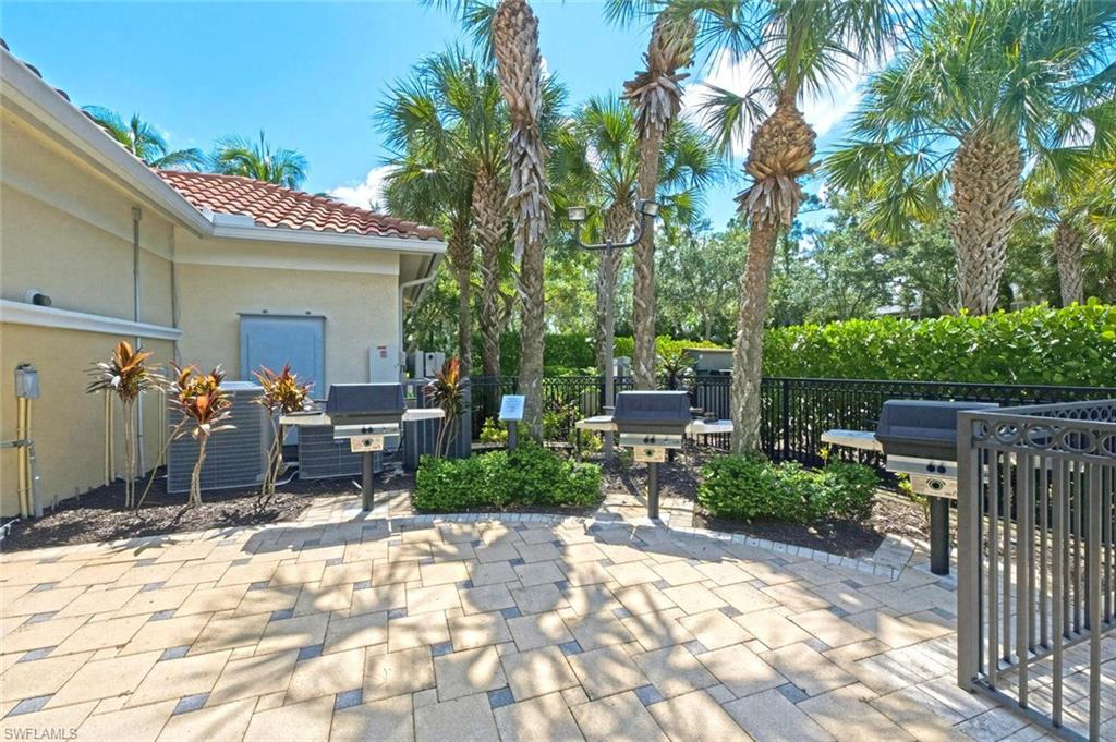 Paved patio with multiple built-in grills, bordered by a black metal fence and mature palm trees