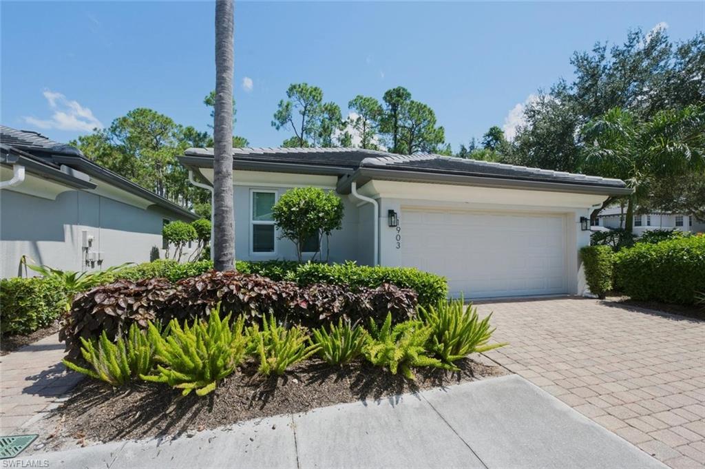 Paver driveway leading to an attached garage, with dense landscaping and a concrete tile roof