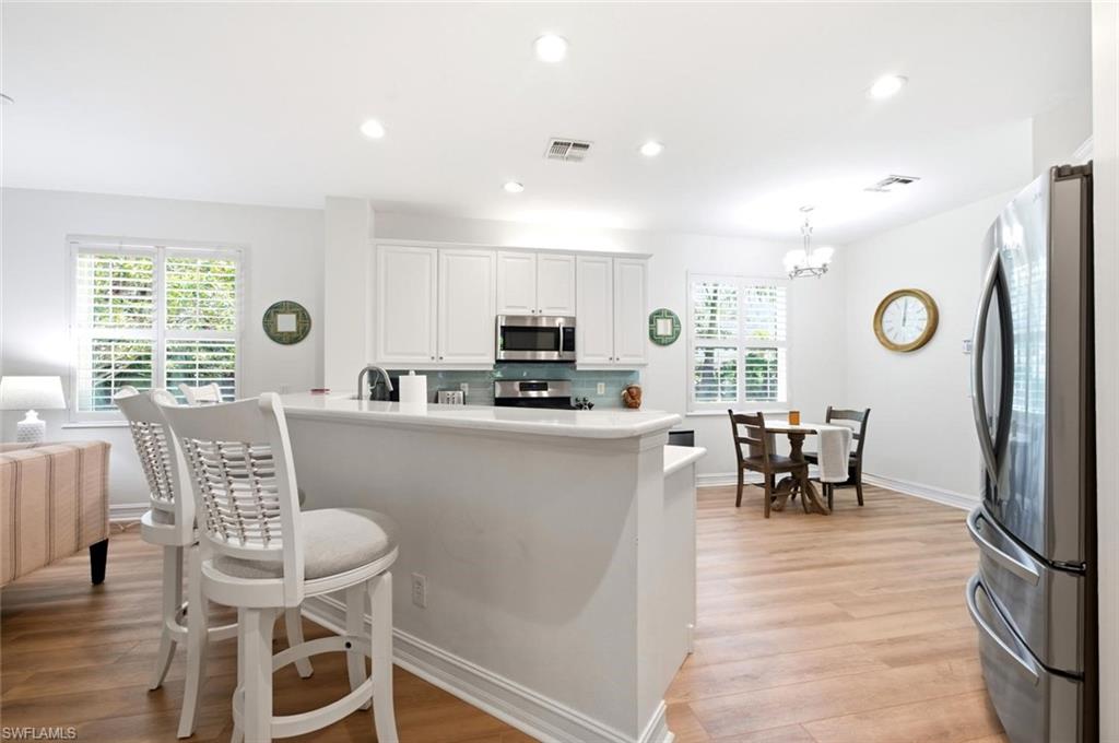 Kitchen featuring white cabinetry, stainless steel appliances, a light blue tile backsplash, and light wood-finish flooring