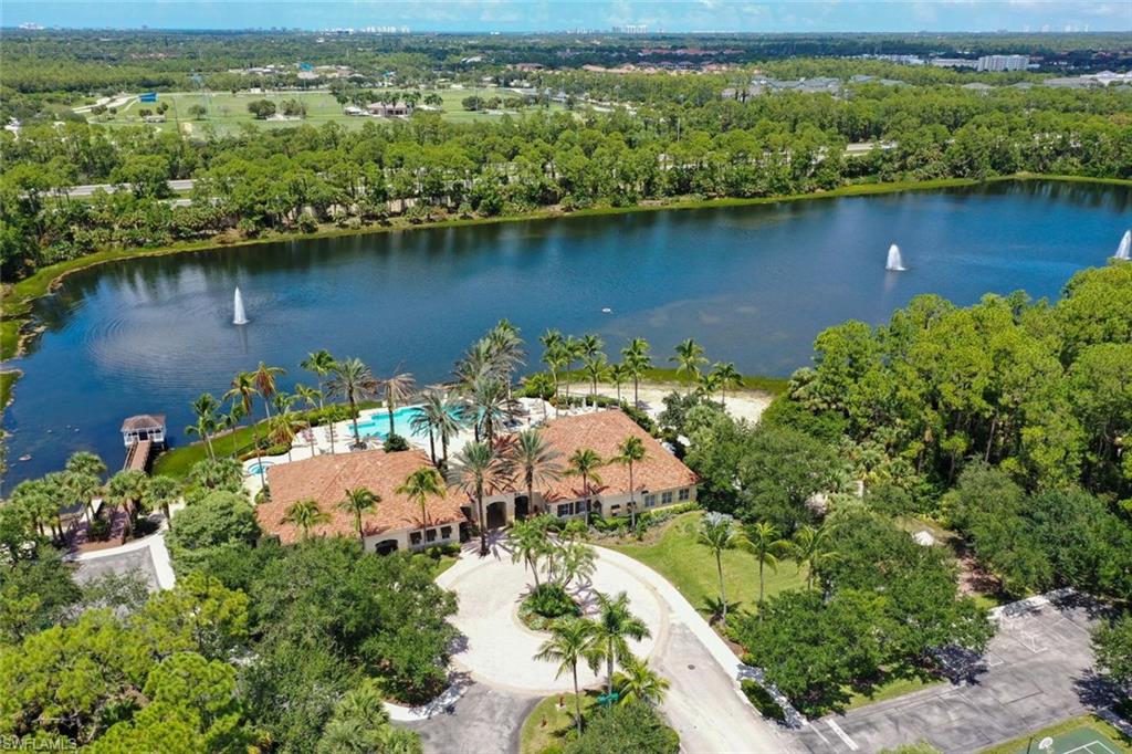 Lakeside property featuring a community pool, mature palm trees, and a private dock with covered seating and beach area