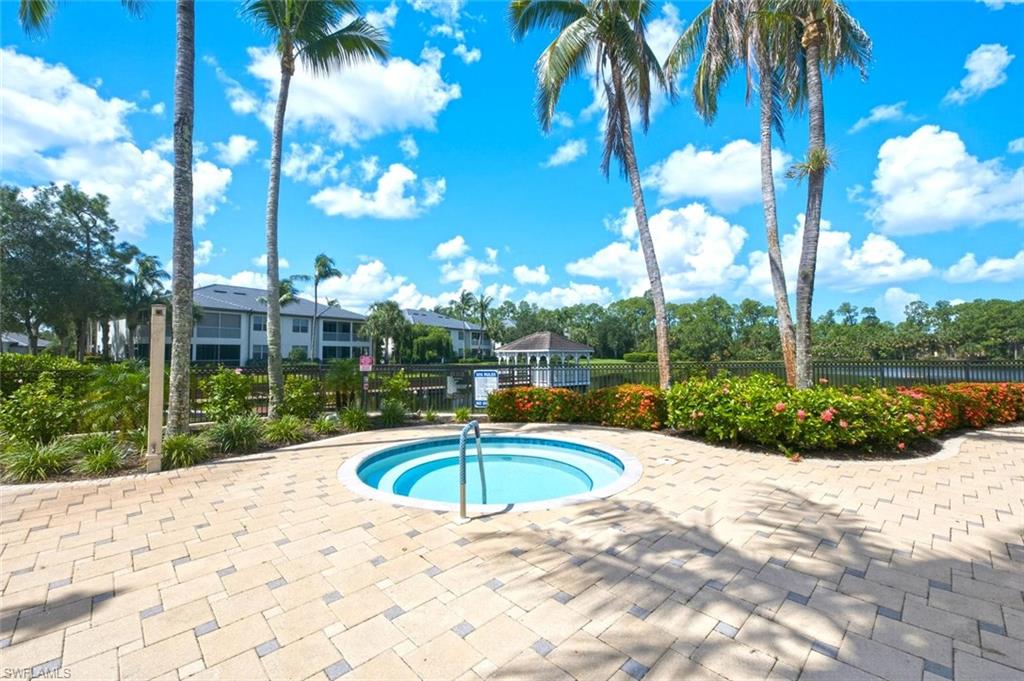 Resort-style outdoor area featuring a circular spa, paver patio, lush landscaping, and mature palm trees