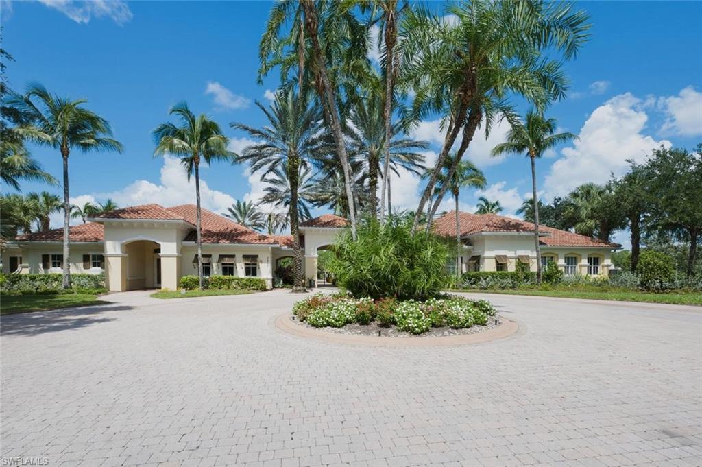 Paver driveway with a central landscaped island, Spanish Colonial architecture, terracotta roof tiles, arched entryways, and lush tropical landscaping