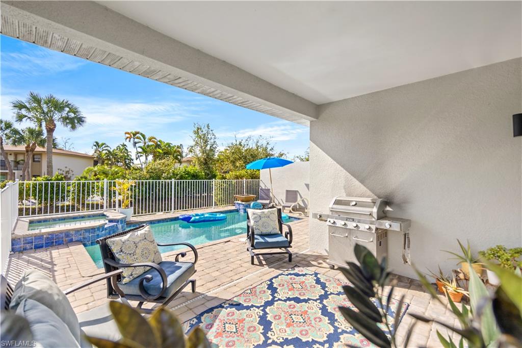 Covered patio with brick paver flooring, outdoor grill, and a fenced swimming pool with an integrated spa