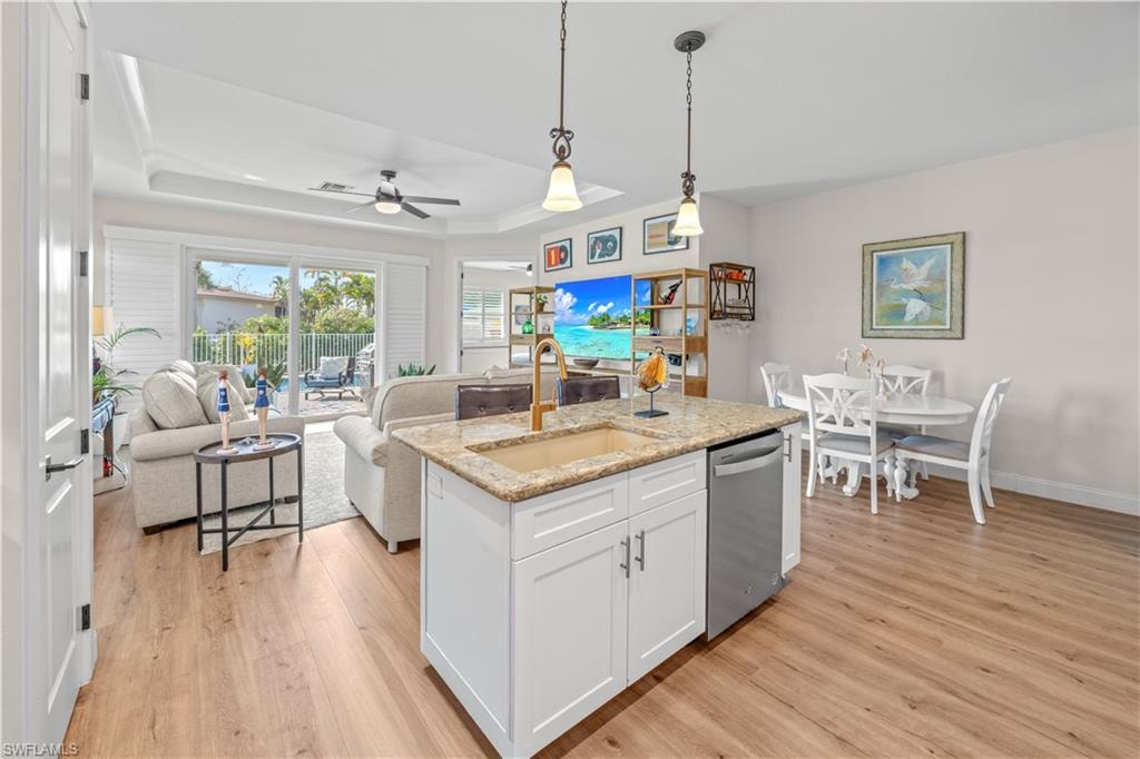 Open-concept layout featuring wood-finish flooring, a kitchen island with stone countertops, white cabinetry, and a ceiling fan