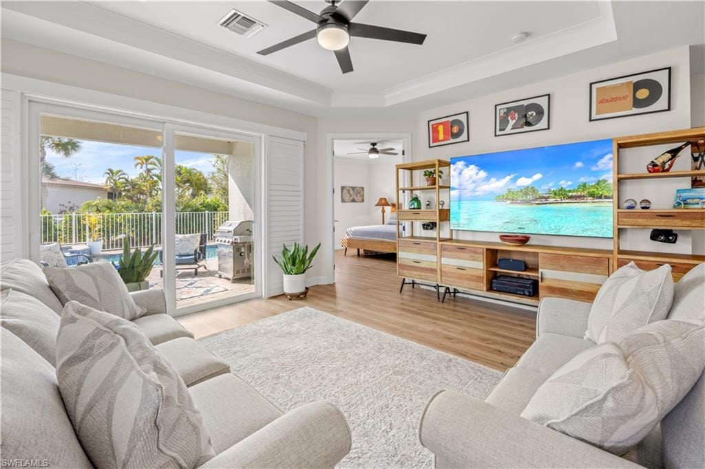 Tray ceiling with recessed lighting and a ceiling fan, wood-finish flooring, and a sliding glass door providing access to an outdoor area with a pool