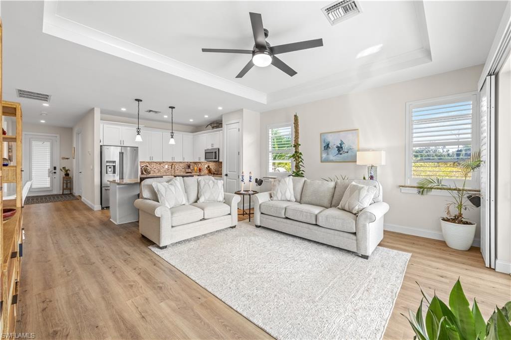 Open-concept living space featuring wood-finish flooring, a tray ceiling, and ceiling fan