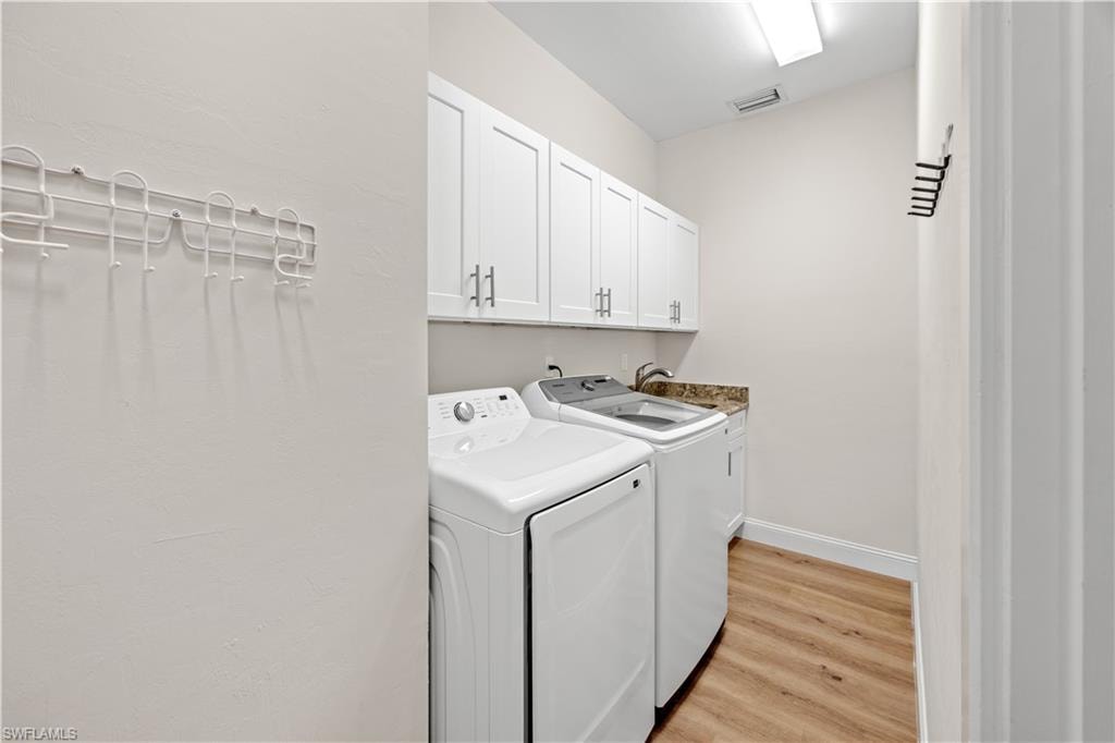Laundry area featuring wood-finish flooring, white cabinetry with silver hardware, a utility sink, and stone-finish countertops
