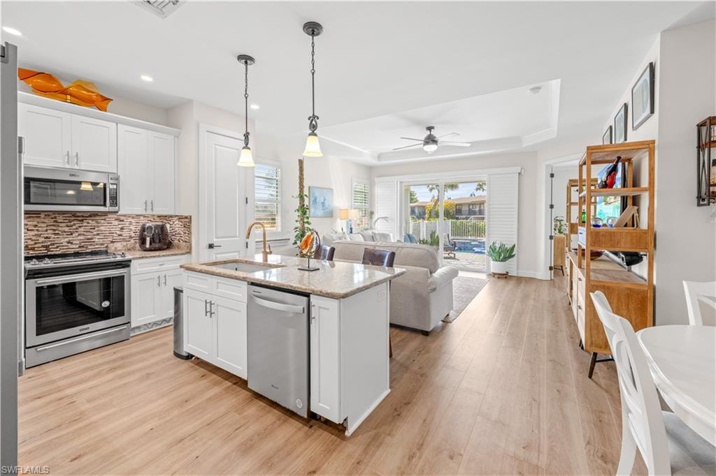 Kitchen with wood-finish flooring, white cabinetry, stainless steel appliances, and a central island with a granite-style countertop