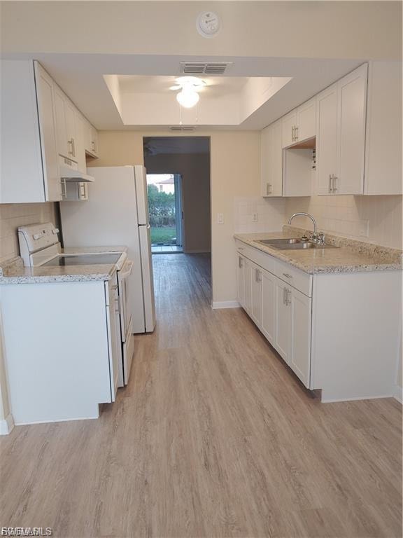 Kitchen featuring light wood-finish flooring, white cabinetry with silver-tone hardware, light-toned speckled countertops, and a white tile backsplash