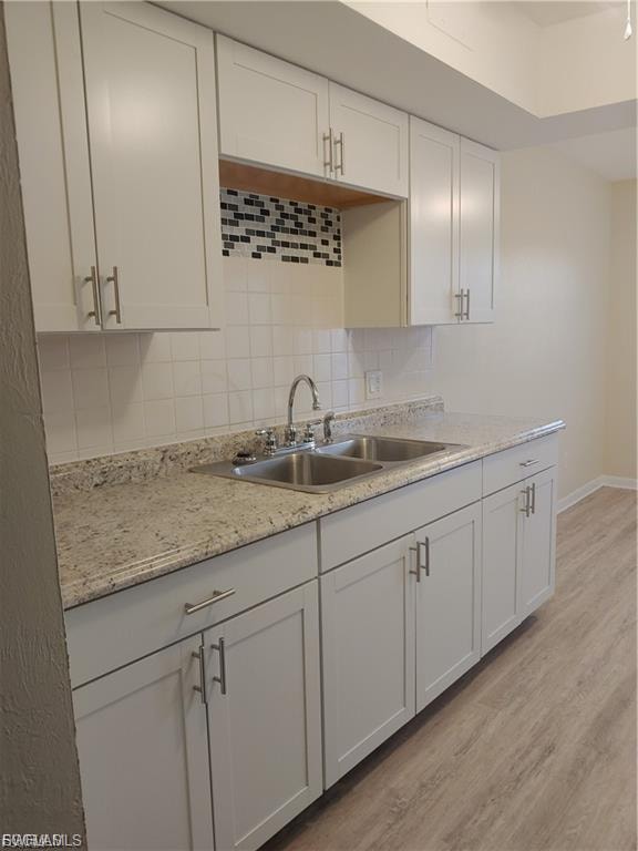 White shaker-style cabinetry with silver-tone hardware, speckled countertops, dual basin stainless steel sink with a chrome faucet, decorative tile backsplash, and wood-finish flooring