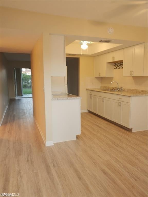 Wood-finish flooring throughout, white kitchen cabinetry, recessed ceiling lighting, and light-toned countertops