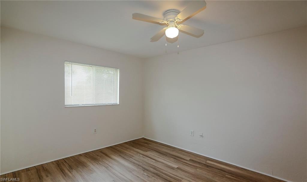 Wood-finish flooring, white walls, single window with blinds, and a ceiling fan with integrated lighting