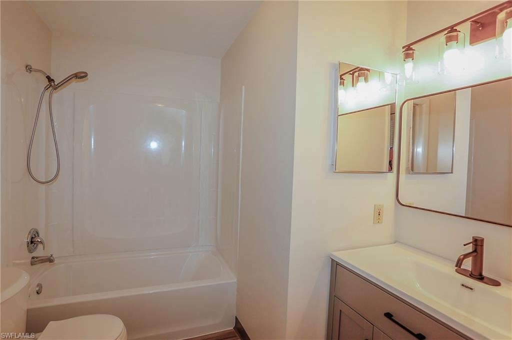 Bathroom featuring a white tub-shower combination with a handheld showerhead, a vanity with a white countertop and integrated sink, a bronze-finish faucet, and two wall-mounted mirrors