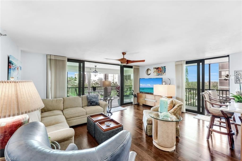 Spacious living area featuring rich wood-finish flooring, a contemporary ceiling fan, and multiple sliding glass doors opening to outdoor spaces with black railings