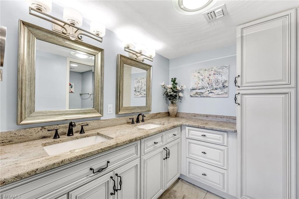 Dual vanity with undermount sinks, stone countertops, white shaker-style cabinetry, and oil-rubbed bronze hardware