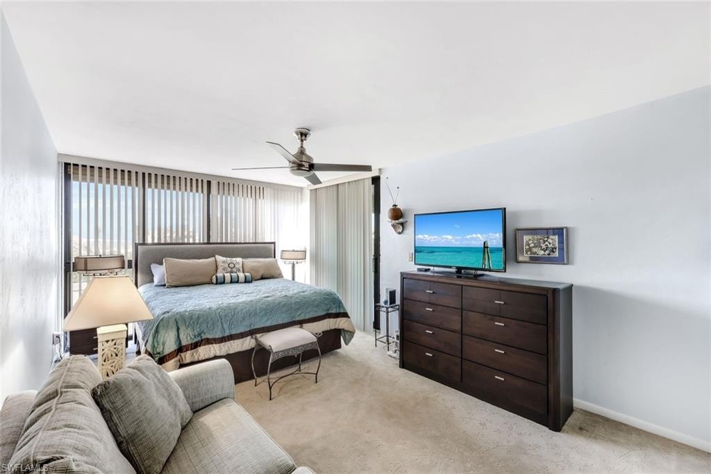 Vertical blinds on expansive windows, ceiling fan, carpet flooring, upholstered headboard