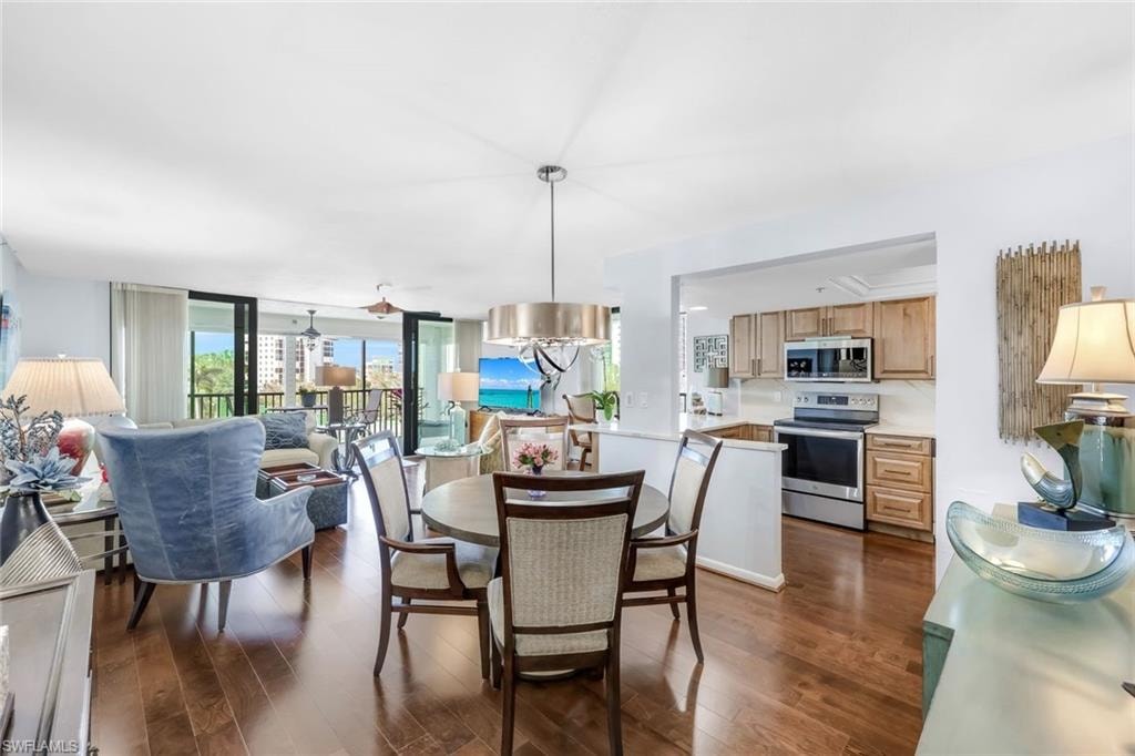 Open-concept living area featuring rich wood-finish flooring, a kitchen with stainless steel appliances, and a dining area with a contemporary chandelier