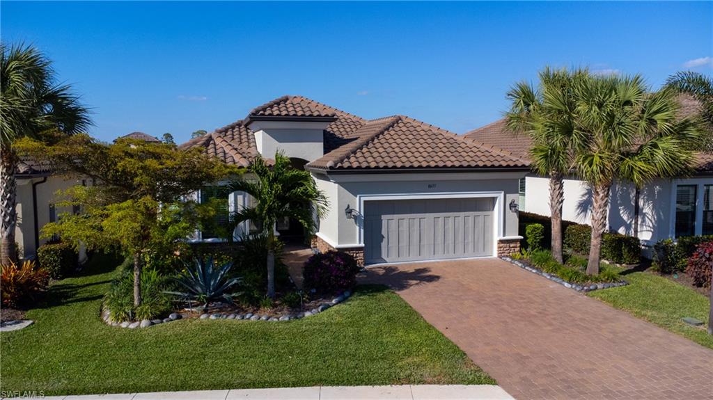 Stucco exterior with a tiled roof, paver driveway, and mature landscaping