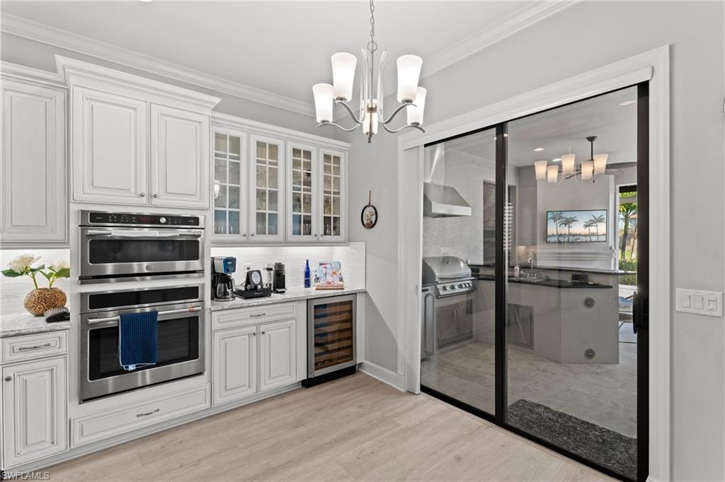 White cabinetry with glass-front accents, stainless steel double ovens, a built-in wine refrigerator, and light wood-finish flooring