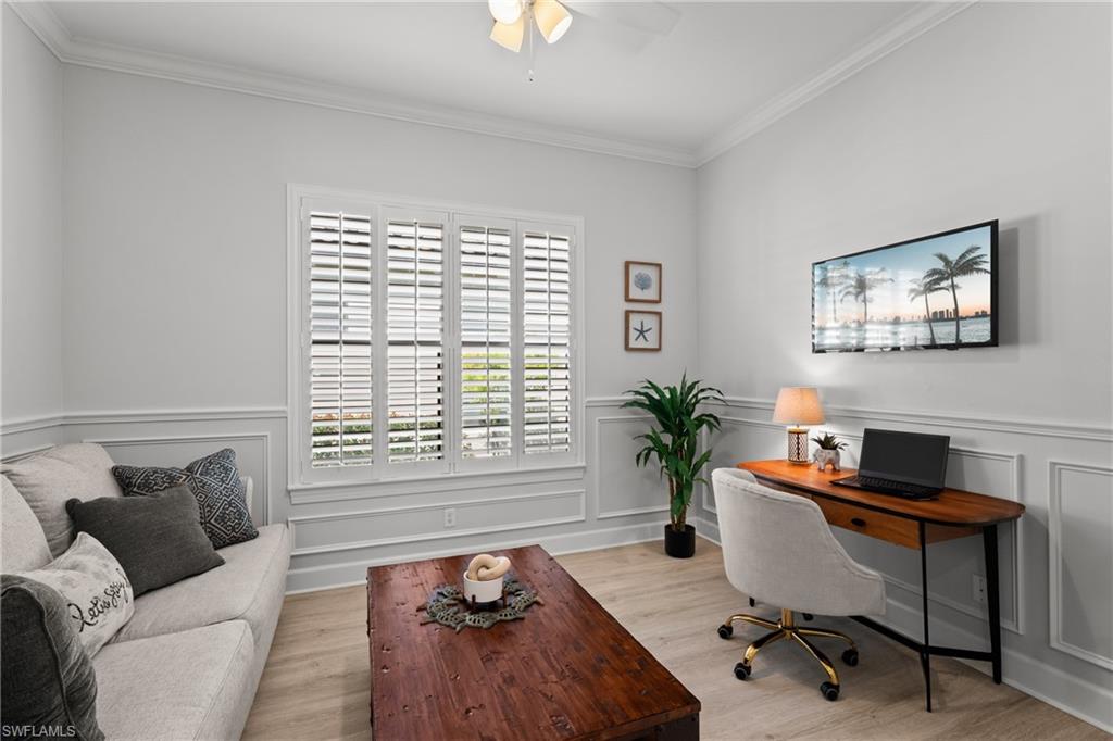 Wood-finish flooring, white plantation shutters, decorative wall paneling, crown molding, and a ceiling fan