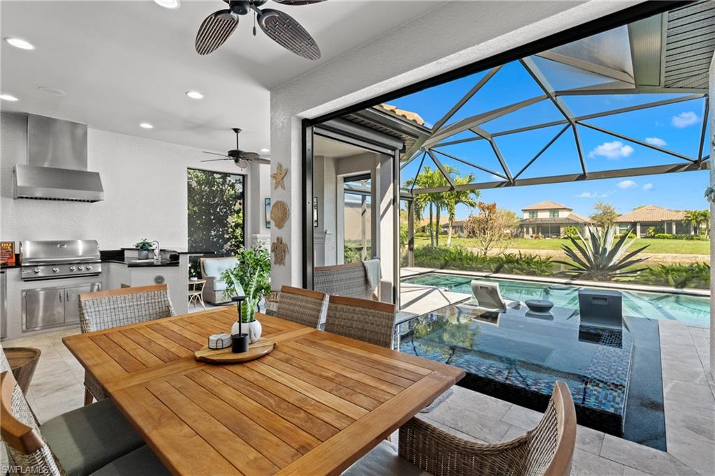 Expansive outdoor living area featuring an integrated kitchen with stainless steel appliances, a screened lanai, and an in-ground swimming pool