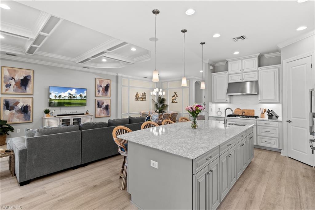 Spacious kitchen island with light-toned countertop, pendant lighting, recessed ceiling lights, white upper cabinetry, and wood-finish flooring