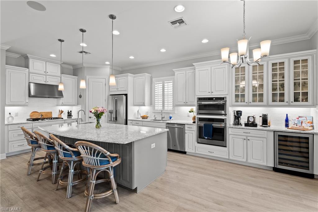 Spacious kitchen featuring white cabinetry, light-toned wood-finish flooring, a large island with granite countertops, stainless steel appliances, and a built-in wine refrigerator
