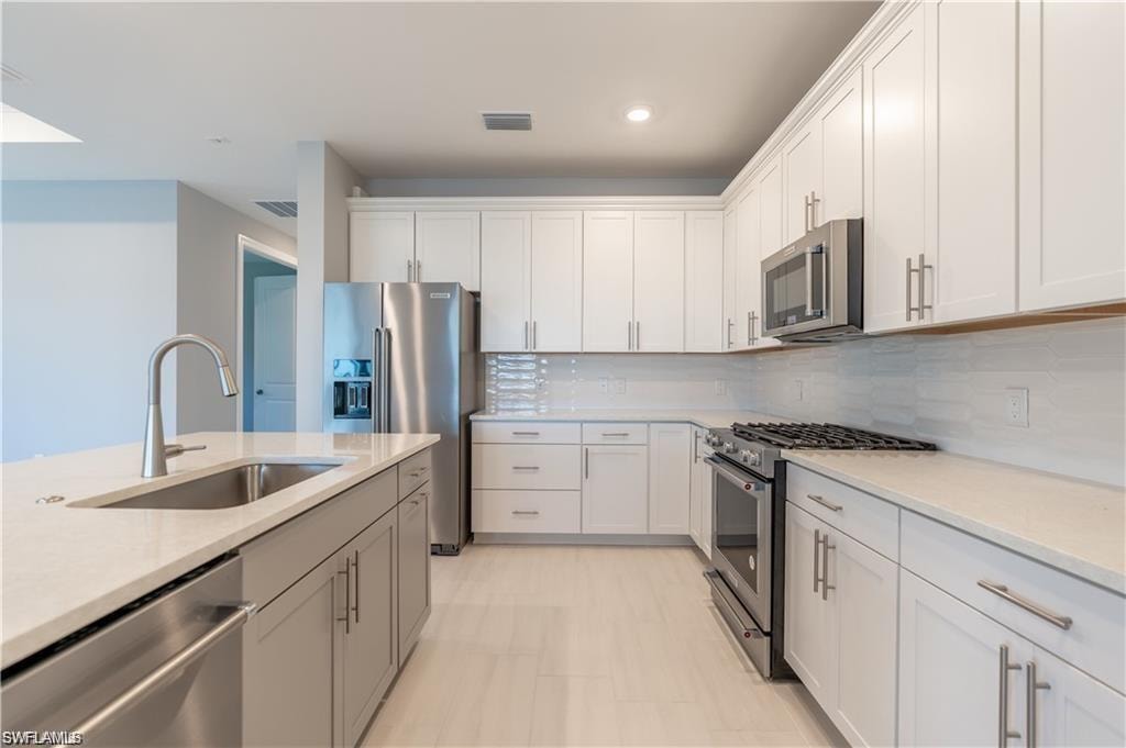 Contemporary kitchen featuring white cabinetry, stainless steel appliances, light-toned countertops, and a full-height tile backsplash