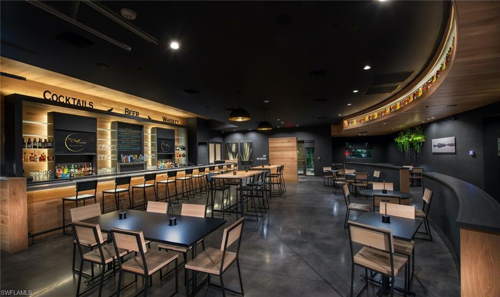 Polished concrete flooring, built-in bar with under-cabinet lighting, wood-finish wall panels, overhead recessed lighting, and a curved architectural wall detail