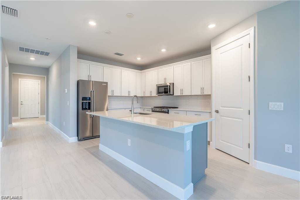 Contemporary kitchen featuring white shaker cabinetry, stainless steel appliances, a light-toned countertop island, and wood-finish flooring