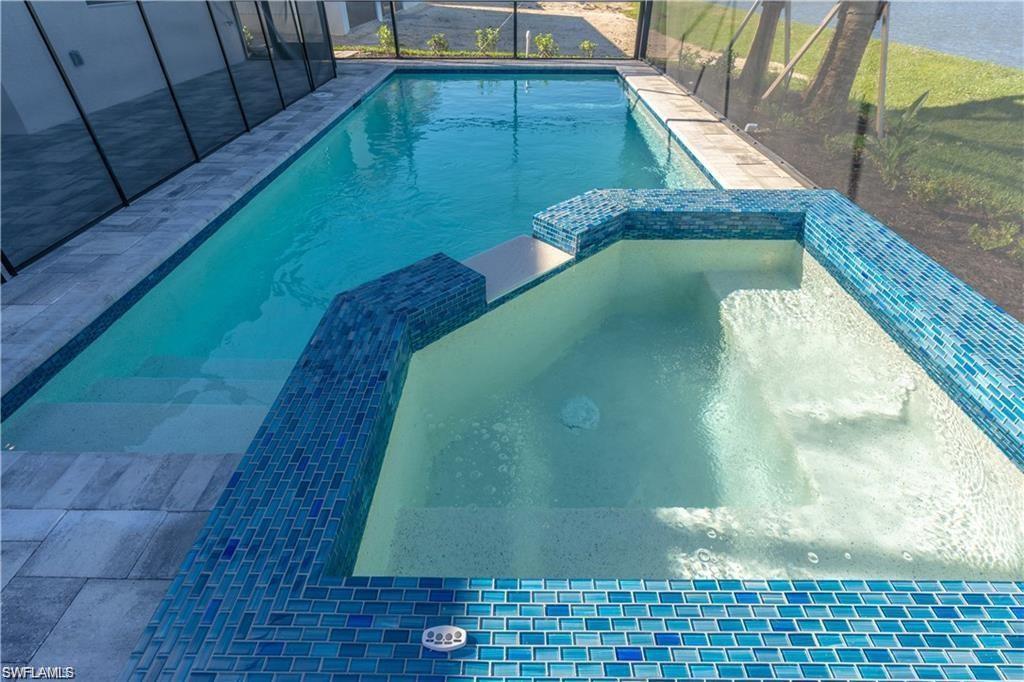 Rectangular swimming pool with integrated spa featuring blue glass mosaic tile, submerged steps, and surrounding grey-toned paver decking