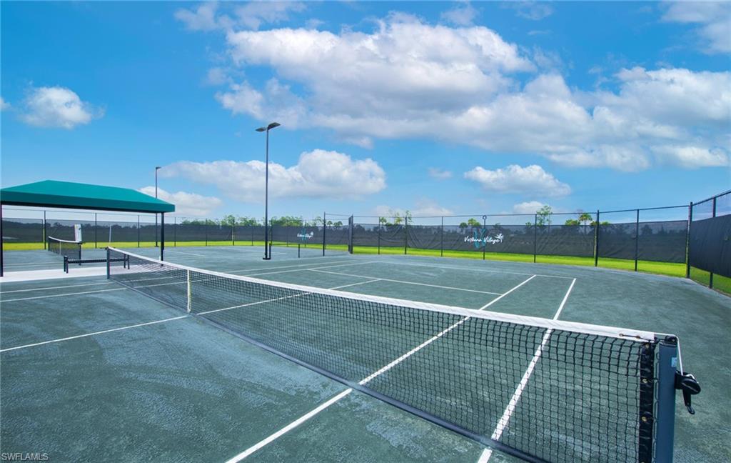 Outdoor tennis courts with multiple playing surfaces, permanent nets, perimeter fencing, and covered seating area