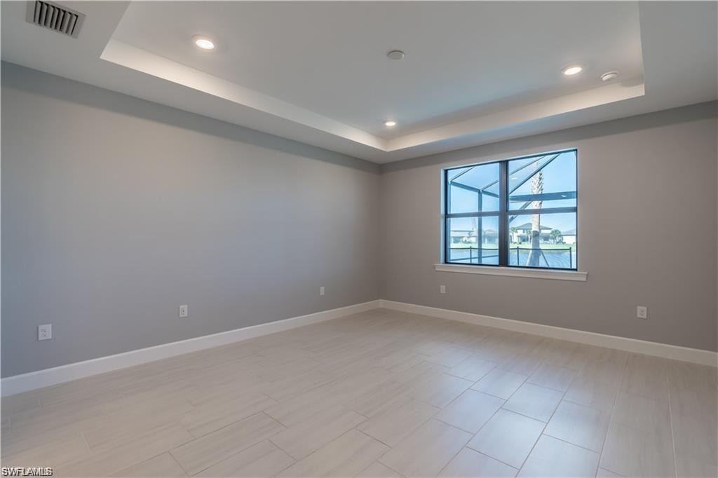 Recessed tray ceiling with integrated lighting, tiled flooring, neutral wall tones, and a large window with water frontage