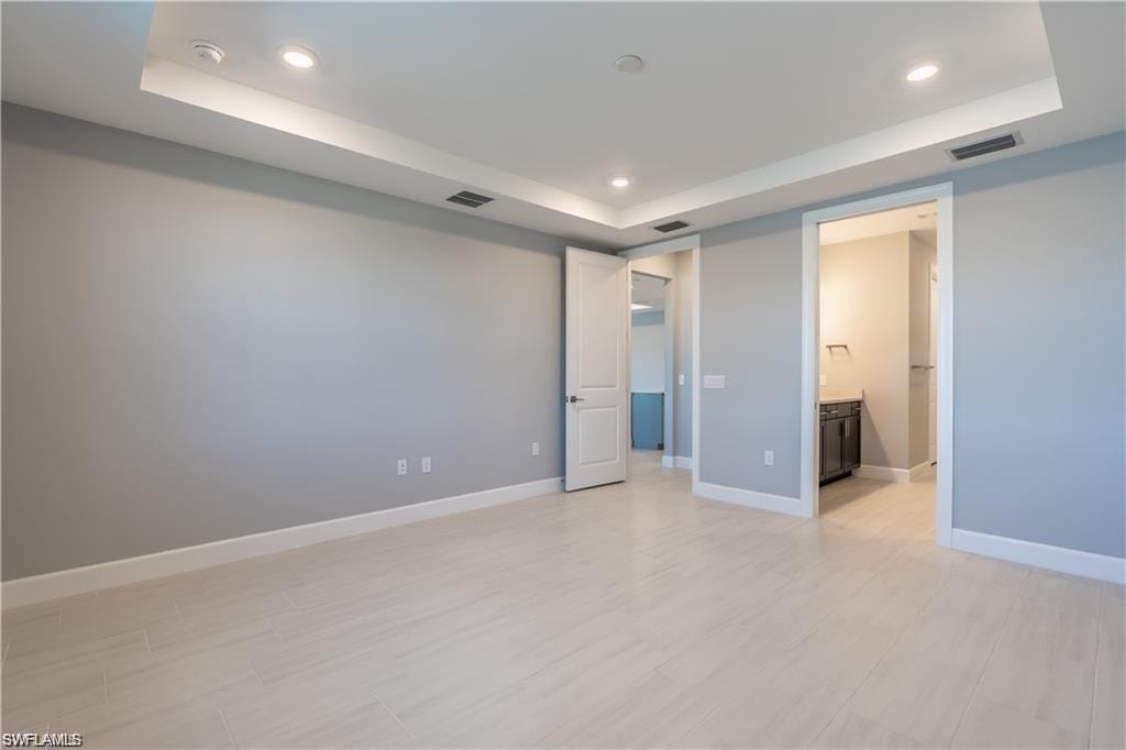 Recessed lighting, tray ceiling, light-toned wood-finish flooring, and white trim