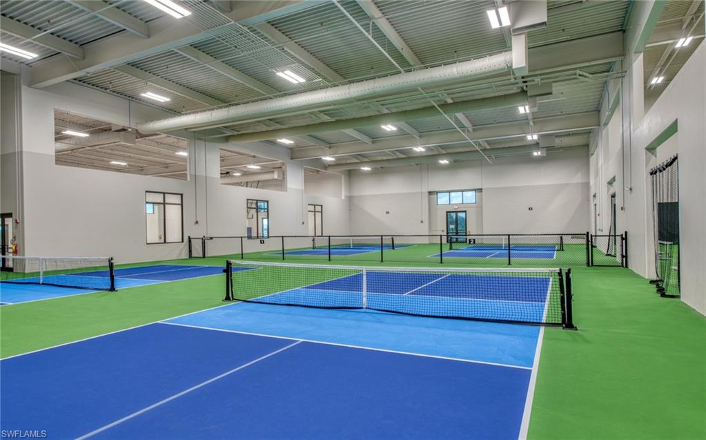 Indoor sports facility featuring multiple courts with blue and green surfacing, high ceilings, and extensive overhead lighting
