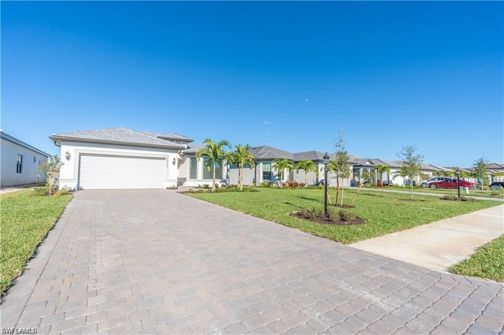 Paved driveway, attached garage, well-maintained lawn, exterior lighting fixtures, and palm trees