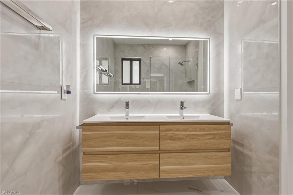 Floating dual vanity with wood-finish cabinetry and white countertop, illuminated by an integrated LED mirror