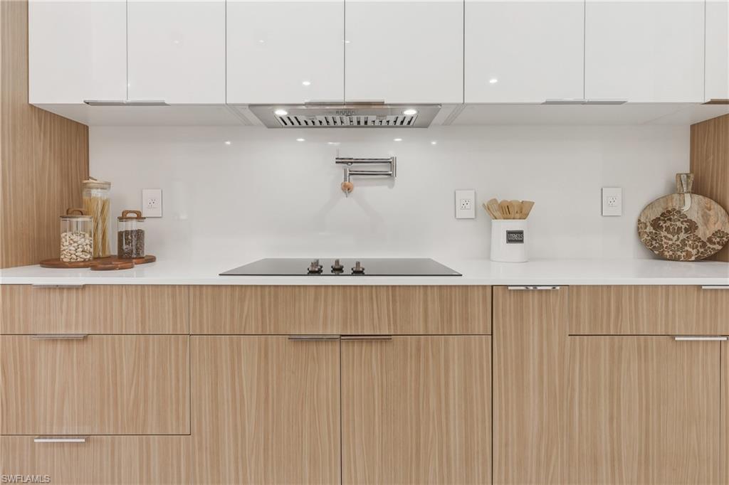 Sleek kitchen featuring white upper cabinetry, wood-finish lower cabinetry, white countertop, integrated cooktop, and pot filler