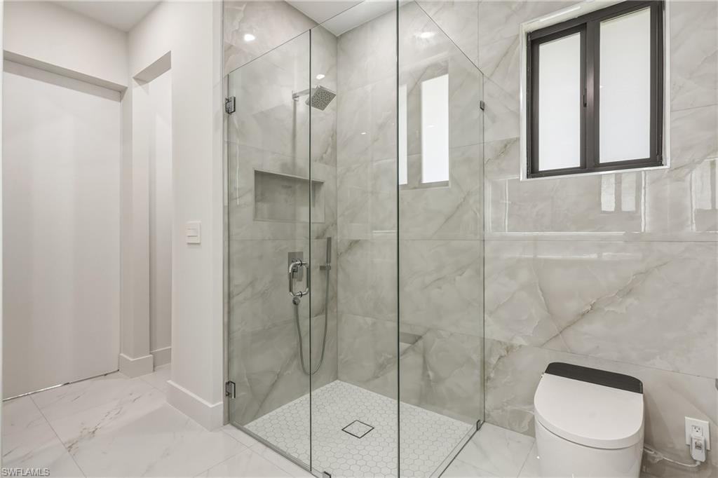 Glass-enclosed shower with a rainfall showerhead, integrated shelf, and hexagonal tile flooring
