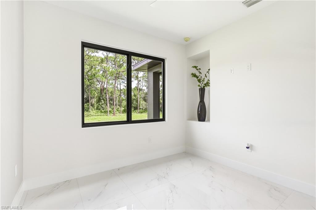 White walls with a recessed niche, large window with black framing, and white marble-look flooring