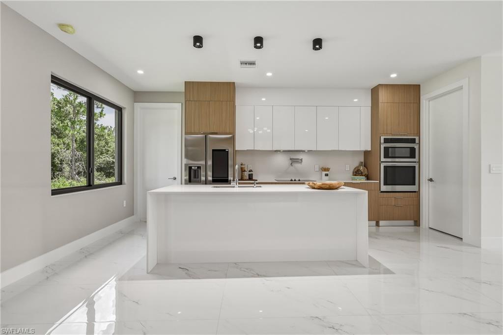 Contemporary kitchen featuring a waterfall island, integrated stainless steel appliances, two-tone cabinetry, and large format polished tile flooring