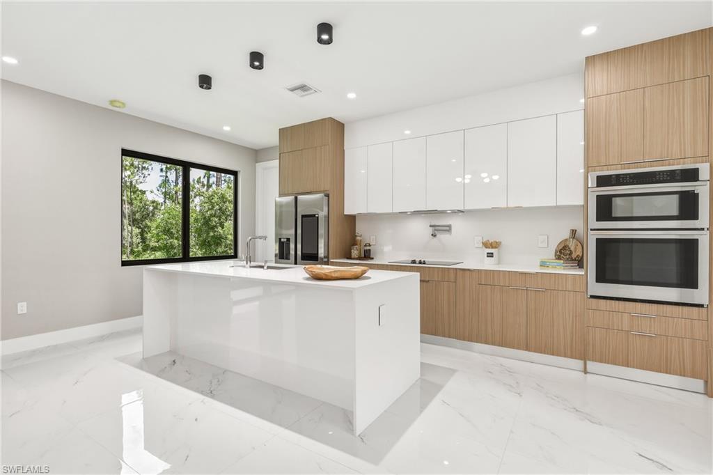 Contemporary kitchen featuring a large central island with a sink, stainless steel appliances, dual-tone cabinetry, and large format white tile flooring